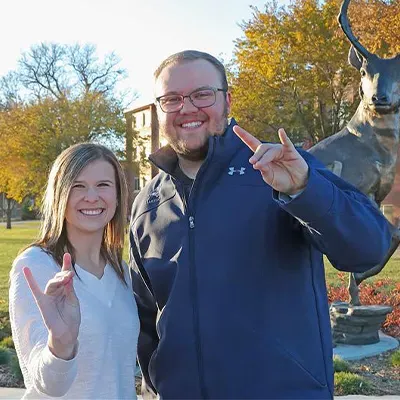two students throw the lopes in front of the loper statue